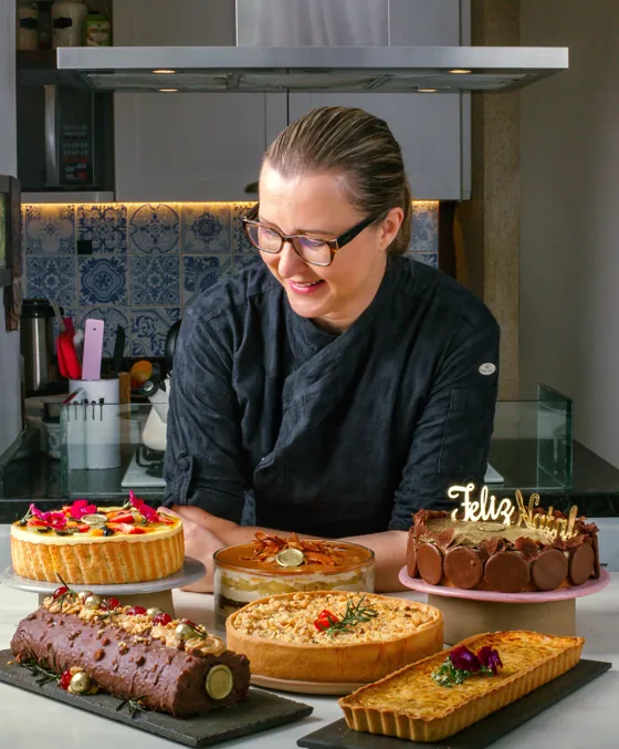 Chef Karyne Iancóski na bancada da cozinha com as seis produções da imersão: Charlotte, pavê, torta holandesa, Bûche de Noël, torta de bacalhau e quiche