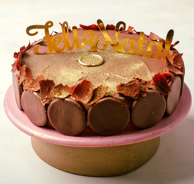 Torta holandesa com ganache, biscoitos de chocolate em volta e topo dourado escrito Feliz Natal