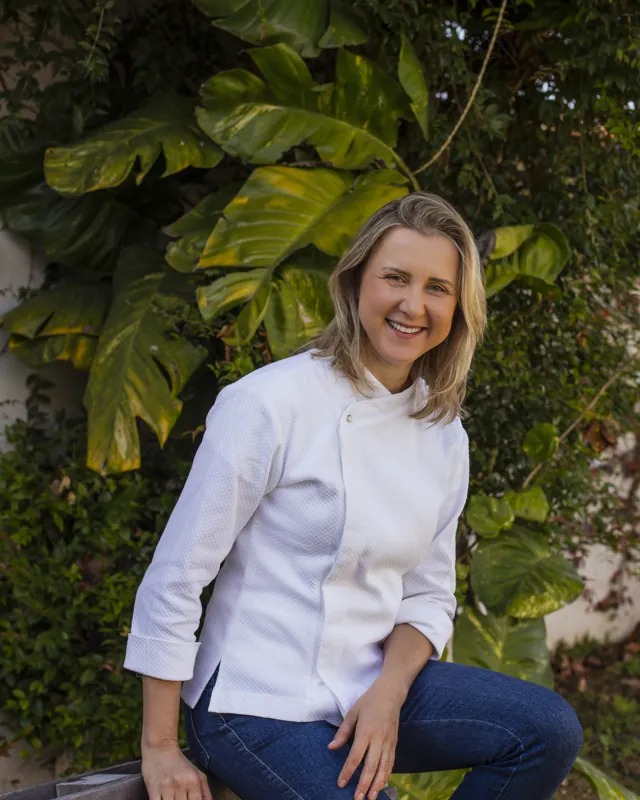 Chef Karyne Iancóski de dólmã branco, sorrindo, sentada no jardim